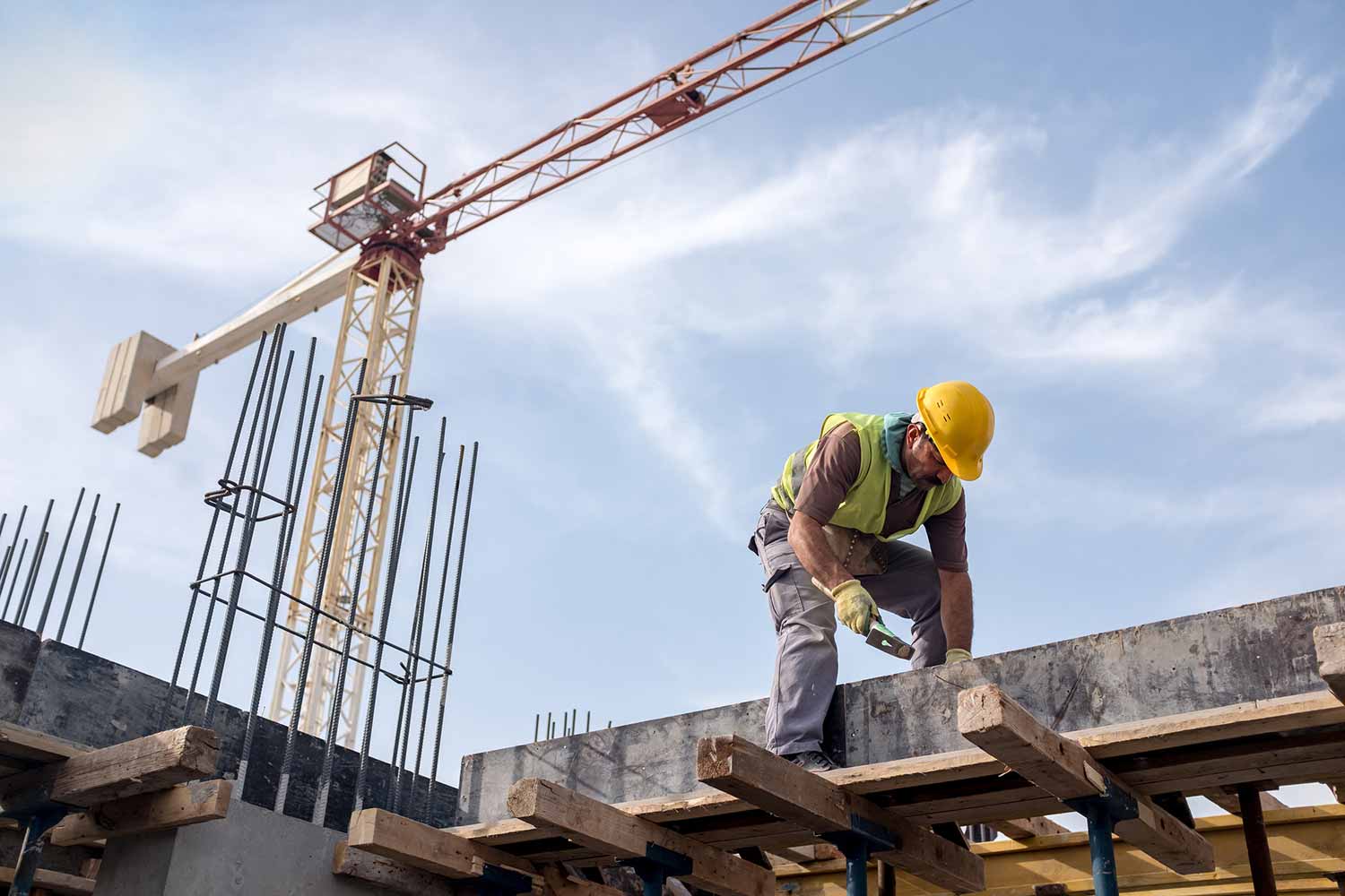 Construction worker on a concrete deck with a tower crane overhead at a building site