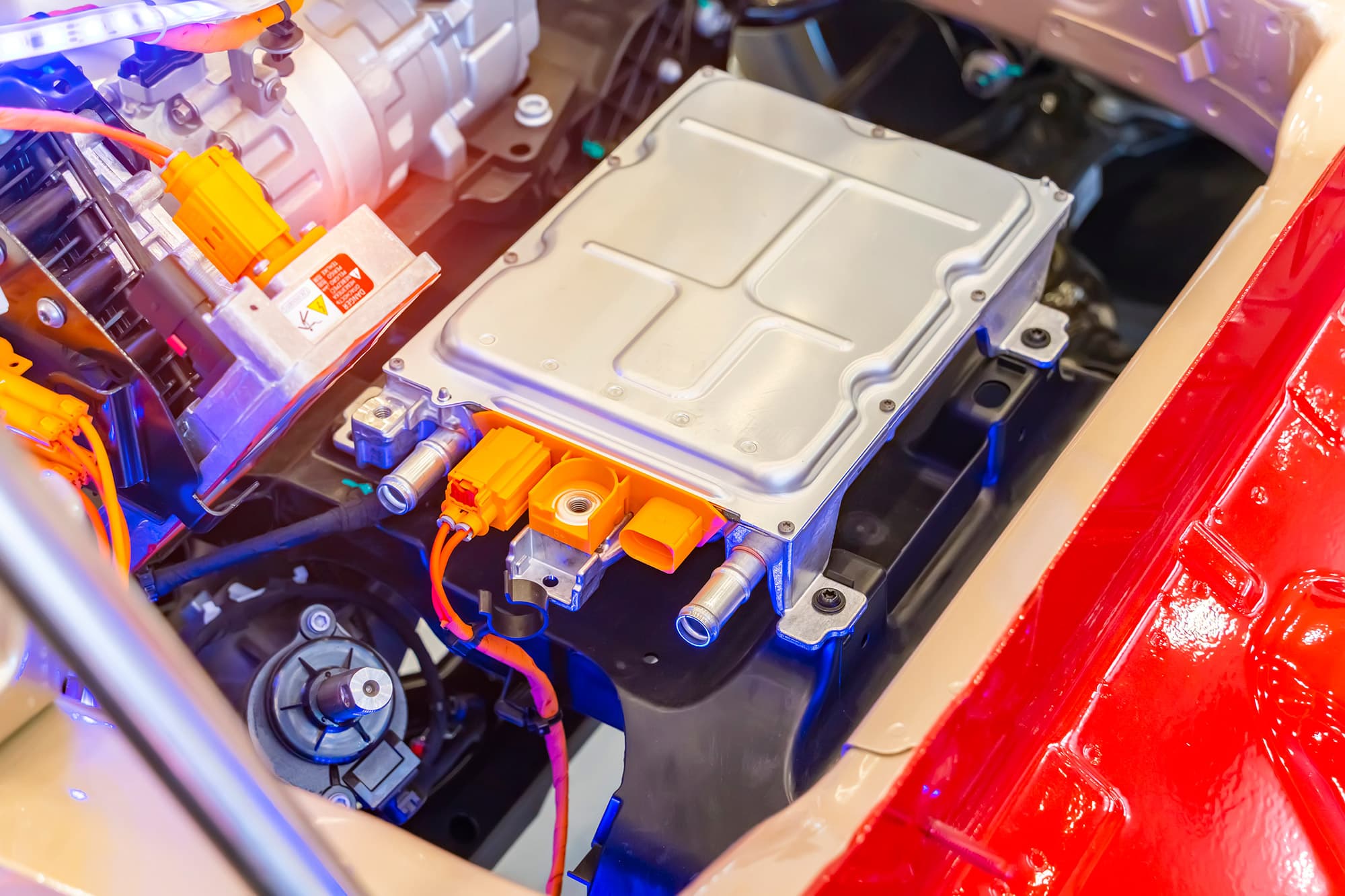 Electric vehicle power module with bright orange high-voltage cables and connectors inside the engine bay of a red car