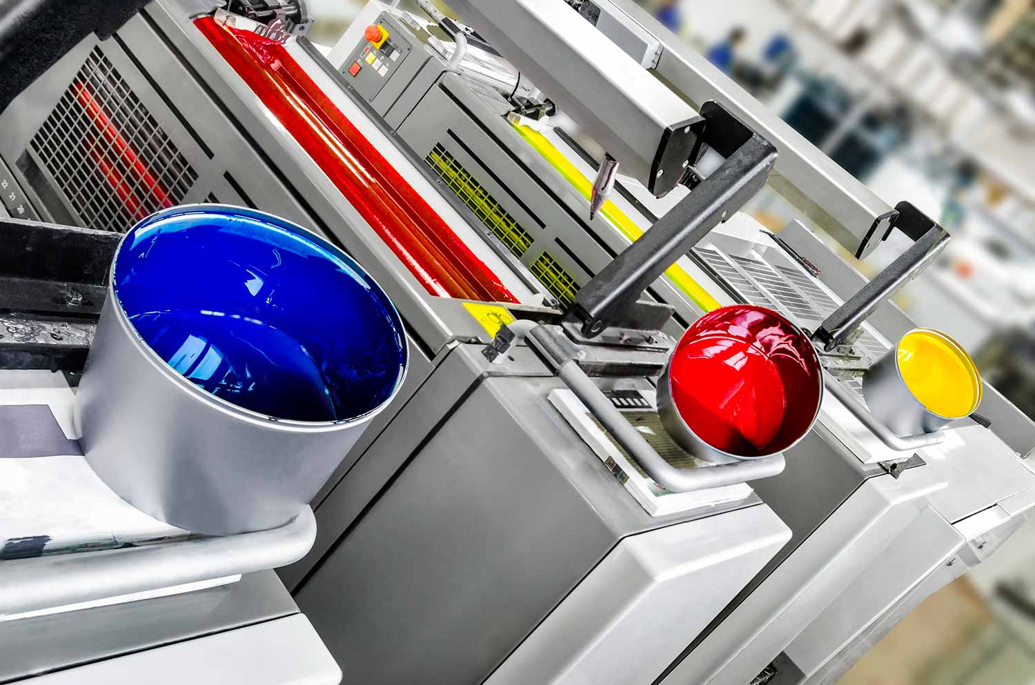 Blue, red, and yellow ink fountains on an offset printing press in a commercial pressroom
