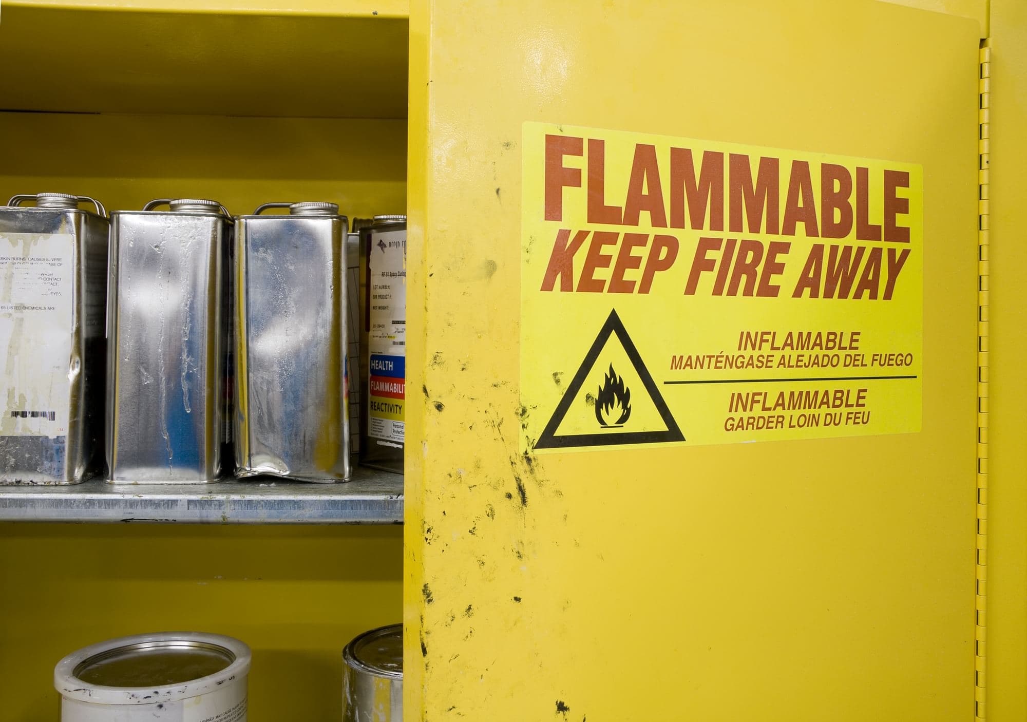 Yellow flammable-liquid storage cabinet with metal containers and a flammable warning label.