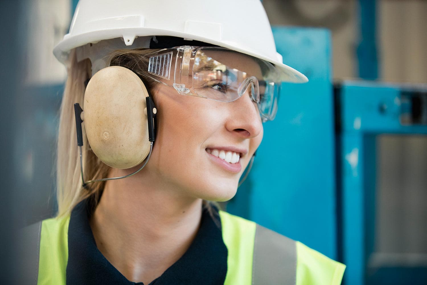 Worker wearing a hard hat, safety glasses, and over-the-ear hearing protection in an industrial facility