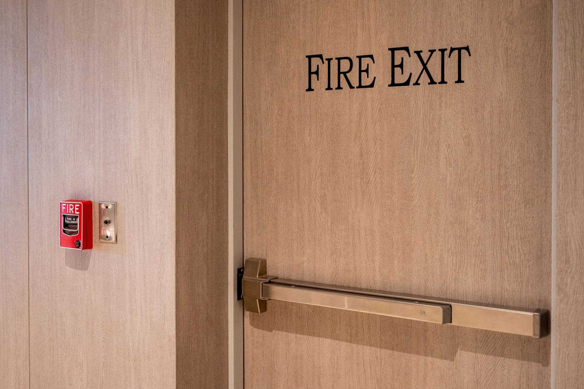 Fire exit door with a panic bar and a wall-mounted fire alarm pull station.