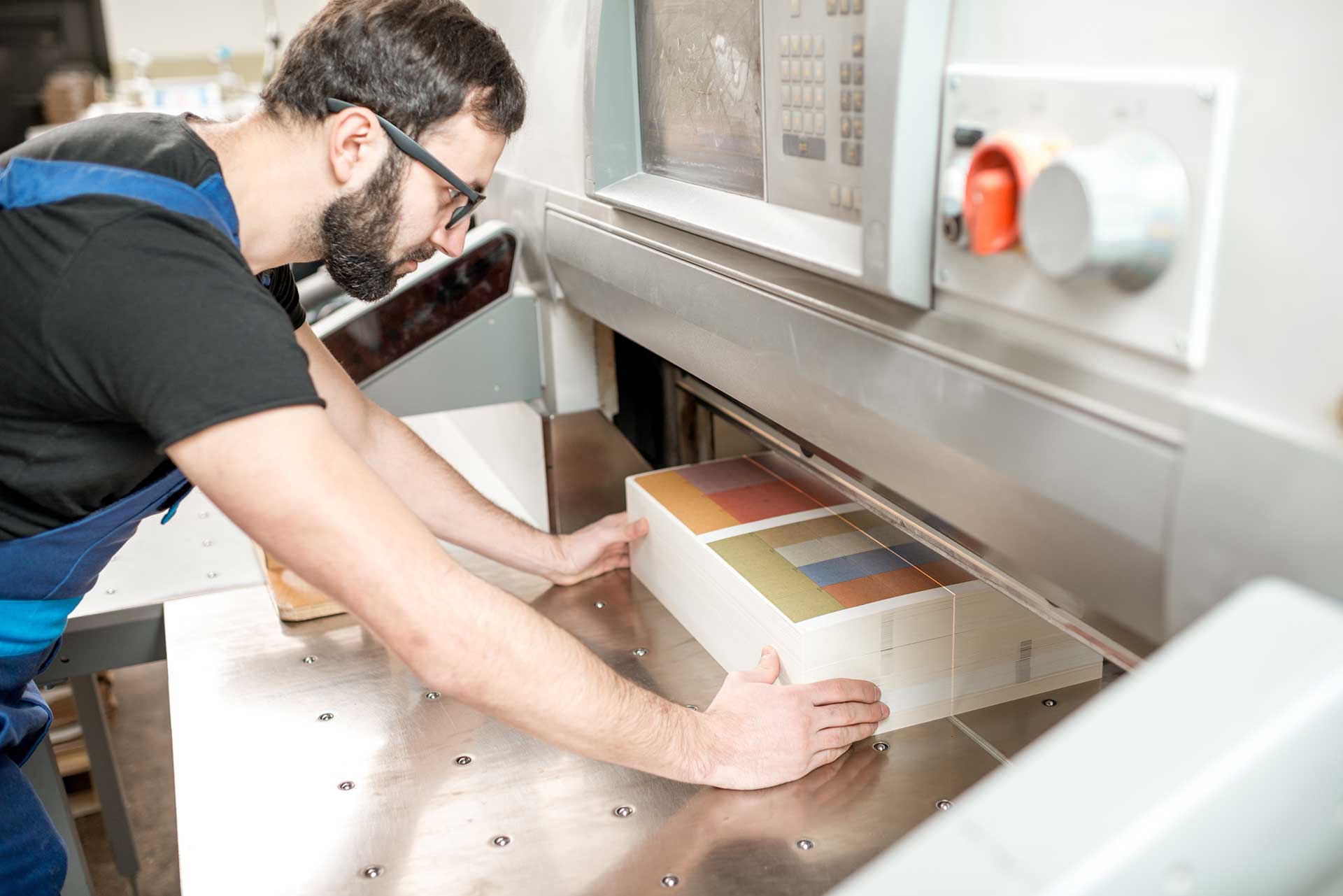Print operator in glasses aligning a thick stack of color-printed sheets in an industrial paper cutting machine
