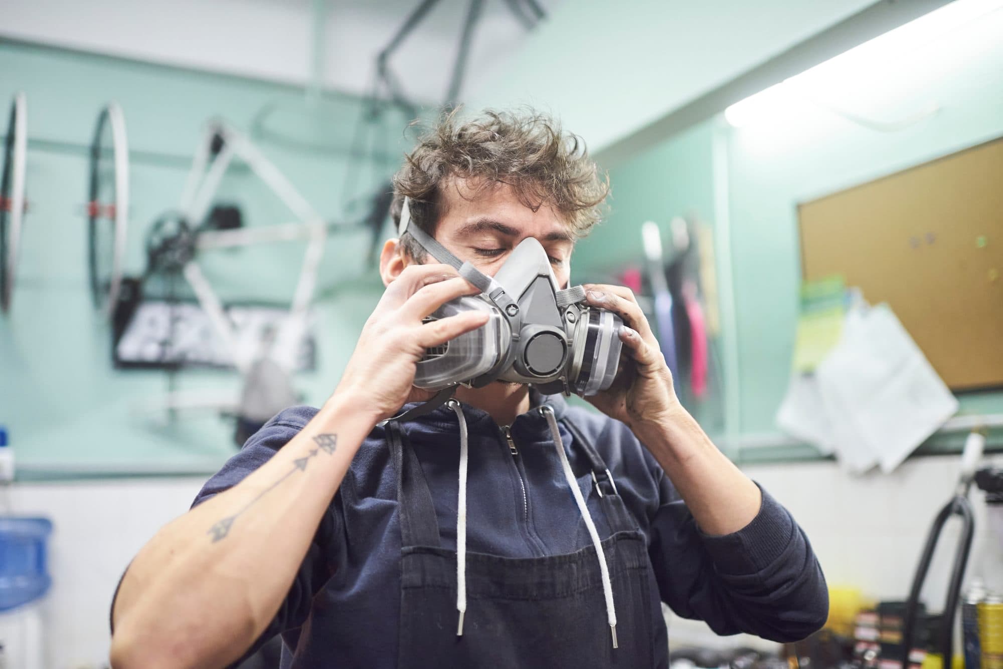 Worker holding a half-face respirator against their face with both hands in a workshop.