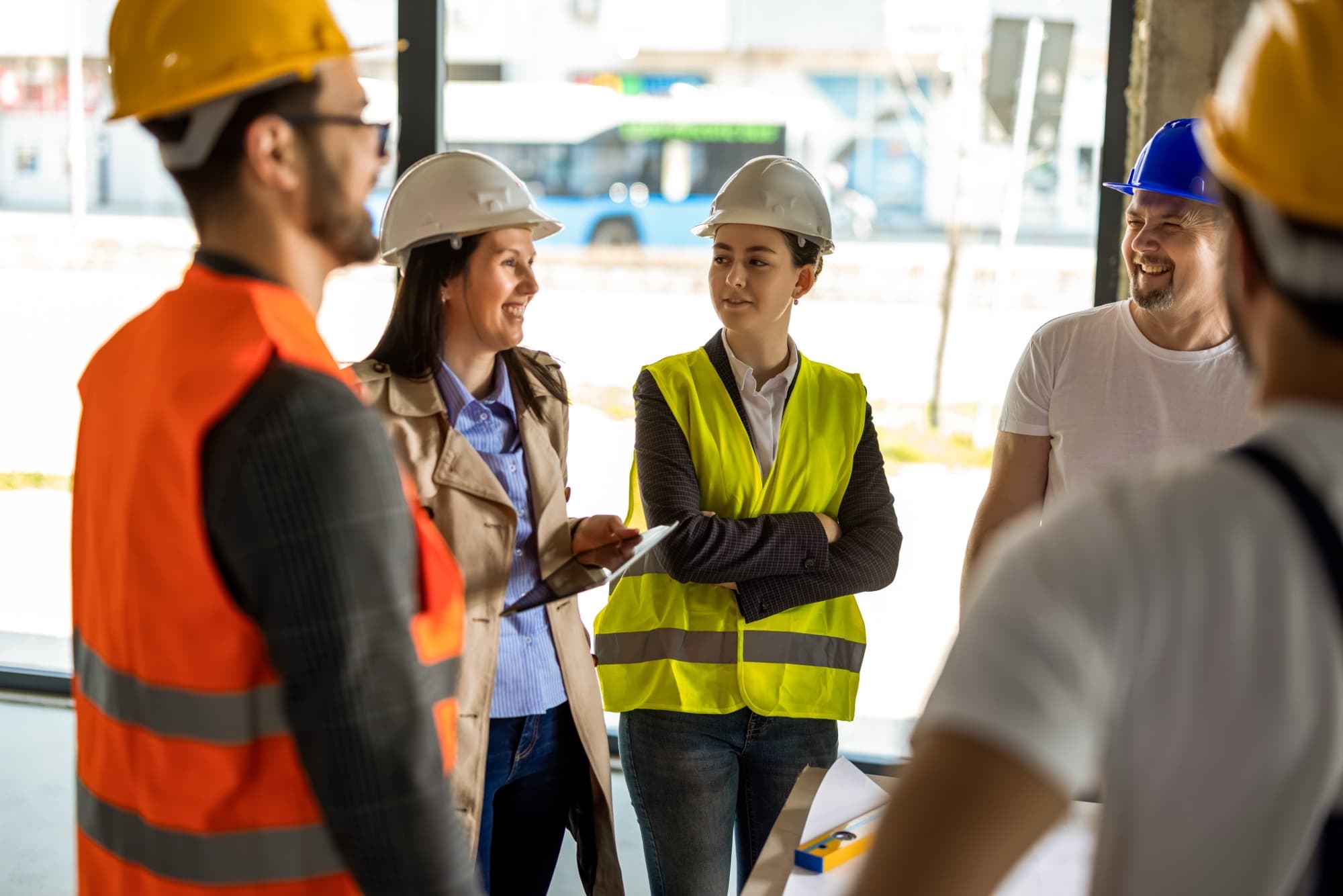 Construction workers in hard hats and safety vests talking together inside an unfinished building