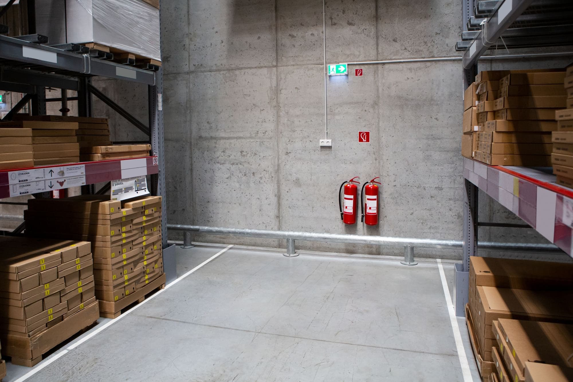 Two wall-mounted fire extinguishers between warehouse storage racks.