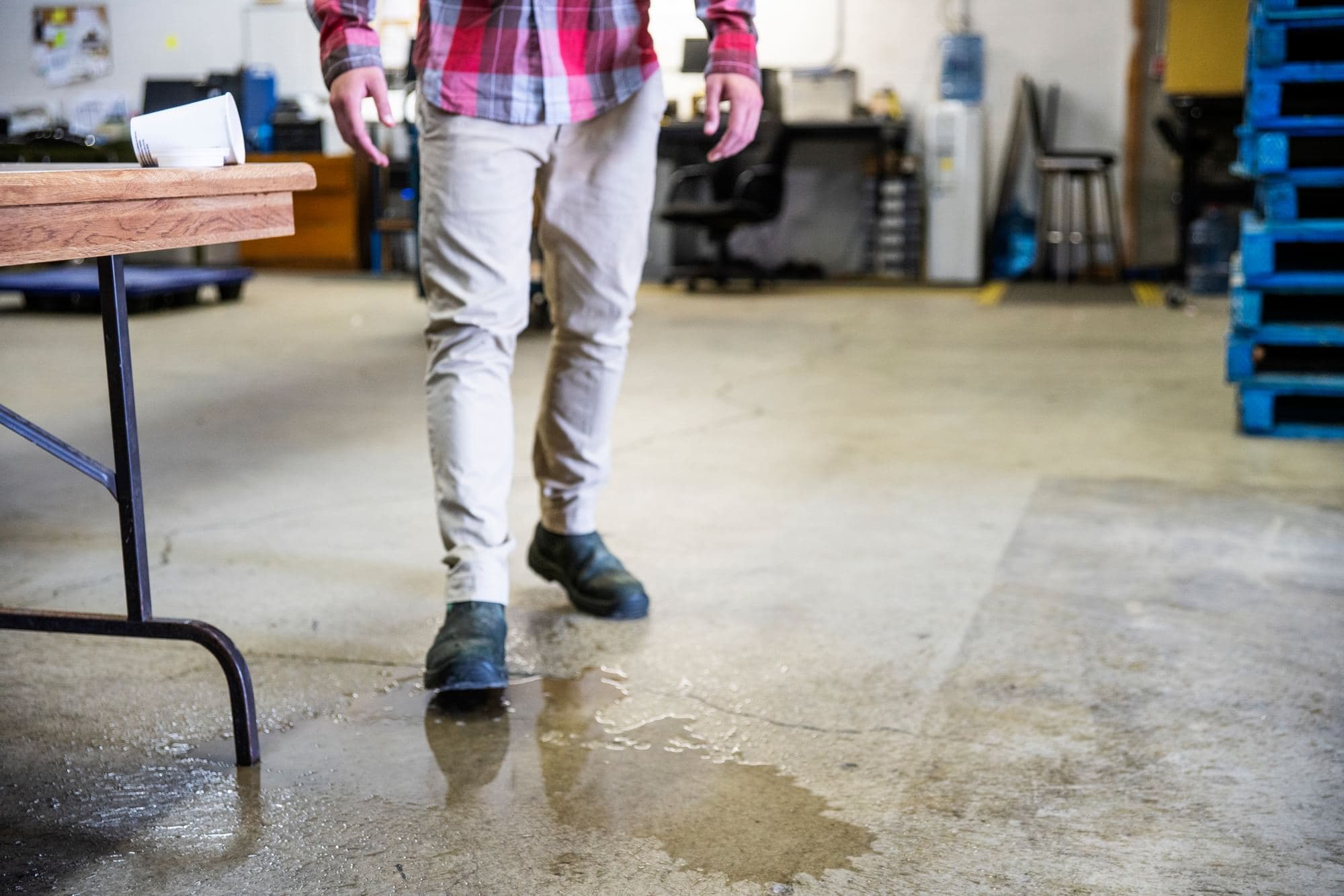 Worker walking near a wet area on a concrete floor in an industrial workspace.