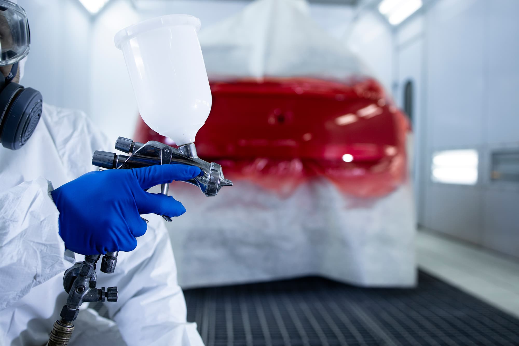 Technician spray painting car with GMG's EHS-compliant collision repair solutions